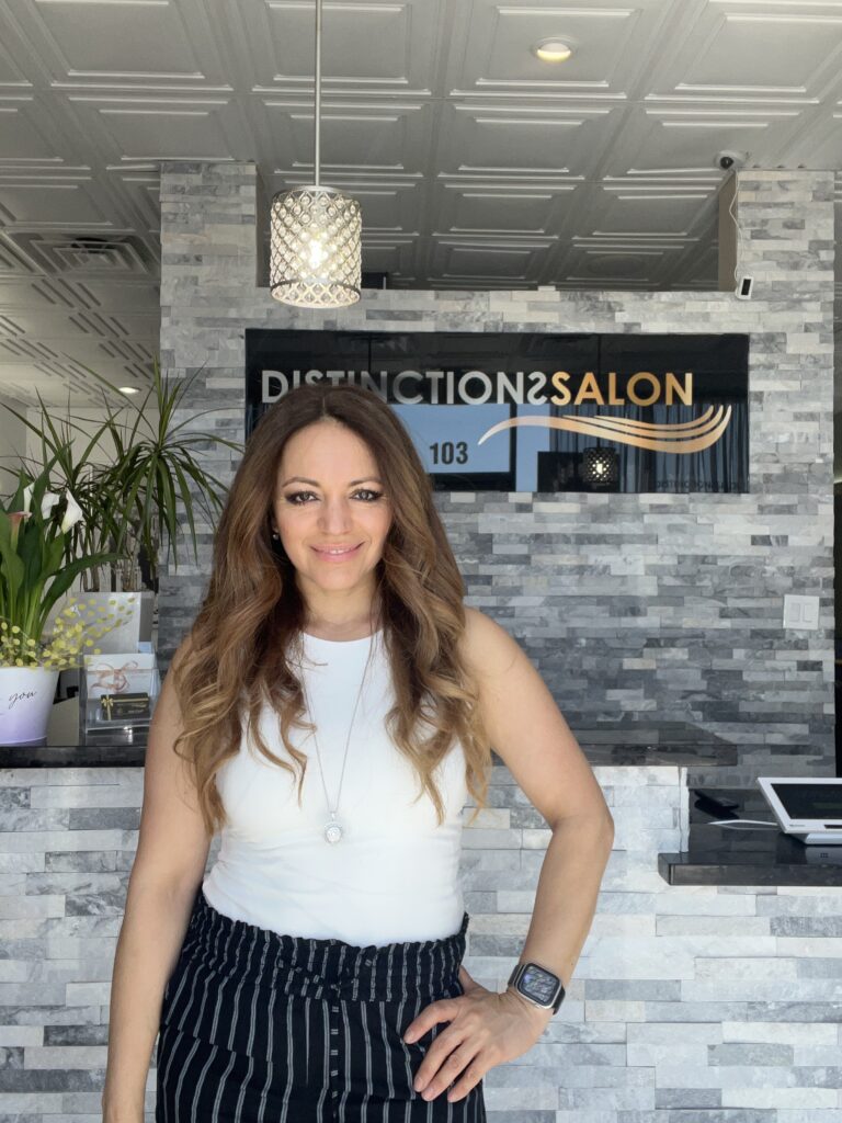 Mia Quintana standing in front of Distinctions Salon logo